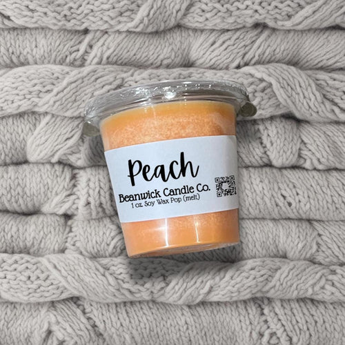 a jar of peach candle sitting on top of a pile of blankets