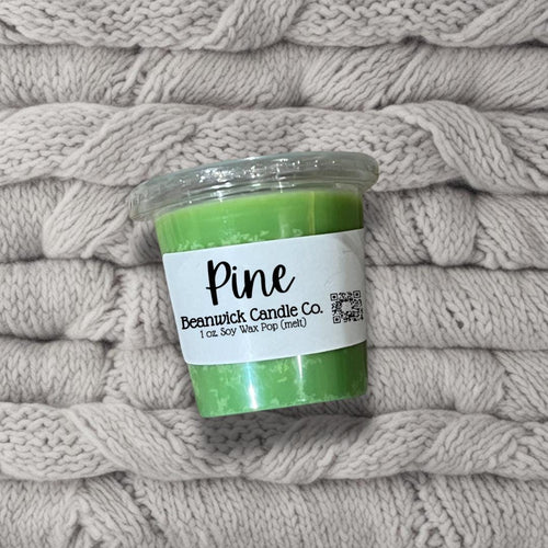 a jar of pine candle sitting on top of a pile of blankets