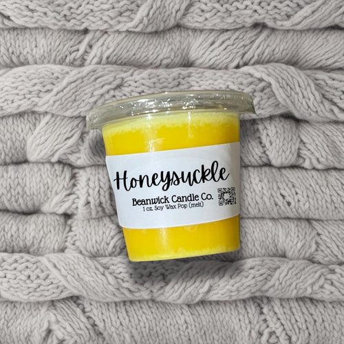 a jar of honeysuckle candle sitting on a pile of blankets
