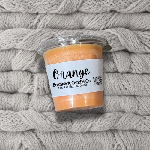 a jar of orange candle sitting on top of a pile of blankets