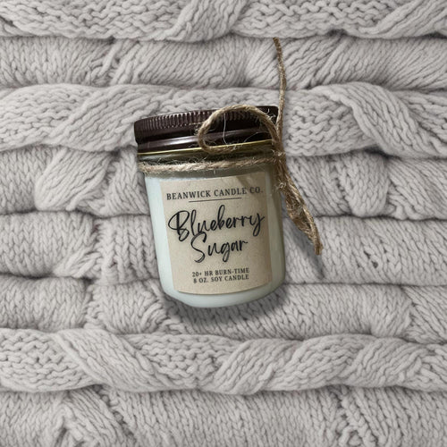 a jar of blueberry season sits on a pile of white blankets