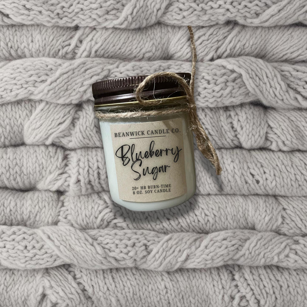 a jar of blueberry season sits on a pile of white blankets