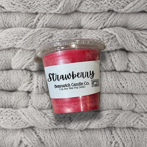 a cup of strawberry candle sitting on top of a pile of blankets