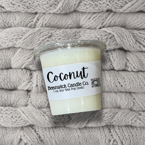 a jar of coconut candle sitting on top of a pile of blankets
