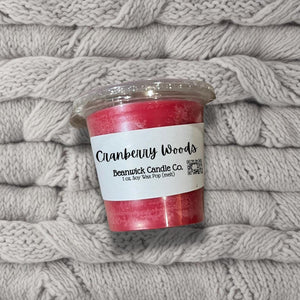 a jar of cranberry woods candle sitting on a pile of blankets